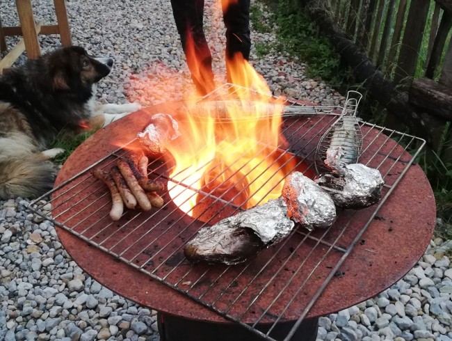 Rustikaler Grill mit Würstchen, Fisch und Folienkartoffeln vor dem Hobbythaus